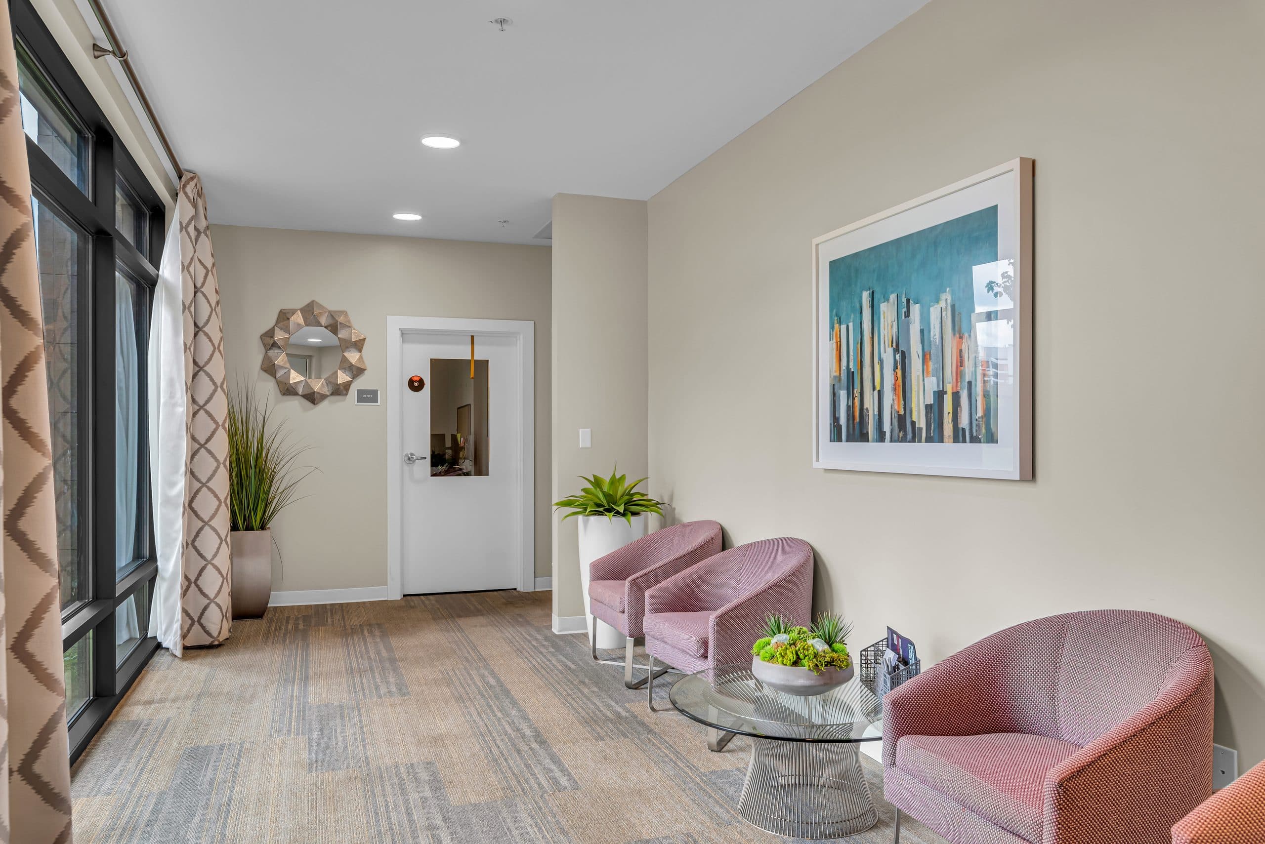 A seating area in the lobby, with pink armchairs, a glass table and a framed city print